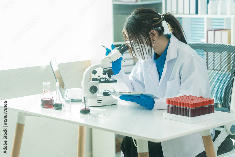 Fototapeta premium Researcher's hand holding blood vessel. Examination of blood vessel in research laboratory. Blood sample wearing blue rubber gloves in laboratory and holding blood sample with microscope next to it.