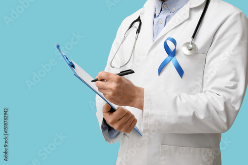 Slika na platnu Male doctor with clipboard and blue ribbon on color background