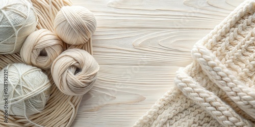 Creamy yarn balls and a chunky knit fabric arranged on a pale wood background