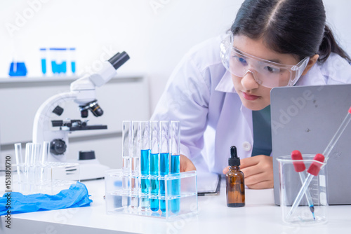 Teen scientist girl conducting science test by carefully evaluating blue solution in laboratory. Science, laboratory, experiment, and research demonstrate academic progress and practical skills.