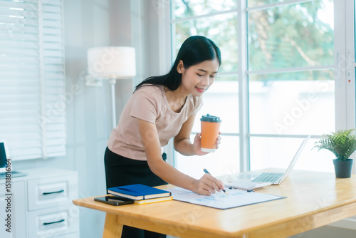 Free Download An Asian housewife relaxes at the table, using her laptop for social media, video calls, and streaming with friends. She enjoys technology and the internet during her leisure time at home. - GFXLoad