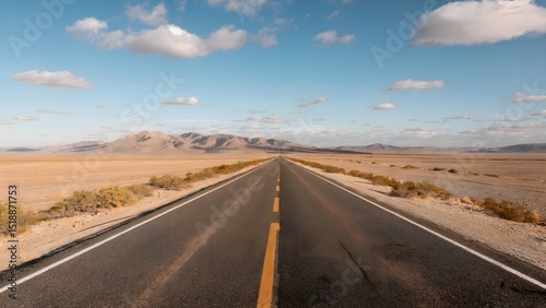 Open road extending towards distant mountains under a clear blue sky with fluffy clouds