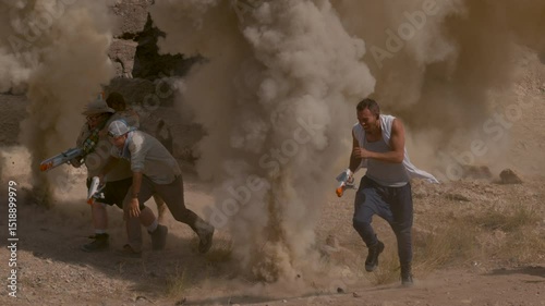 Group with bright toy guns running away as dust explosions go off around them, slow motion shot