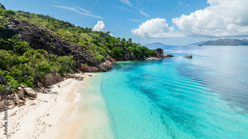 Fototapeta premium A tranquil beach with vibrant turquoise water and soft white sand surrounded by lush greenery. Curieuse, Seychelles.