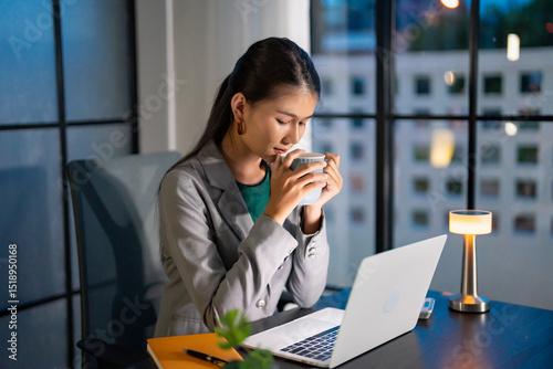 Alone Working Late at Night. Asian business woman at workplace in office late night work at a desk in a dark office working on a laptop late in the evening..