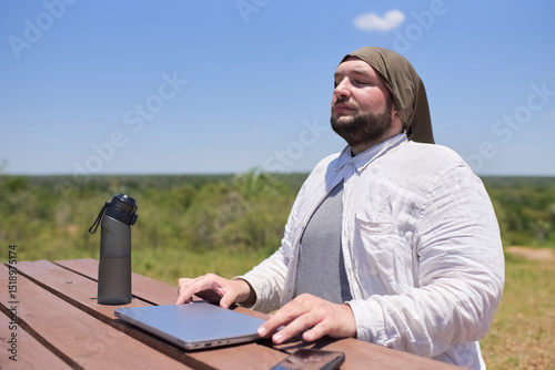 Young Hispanic man closes his laptop after finishing his work, he is outdoors in a sunny natural environment. Concept: digital nomad working remotely while traveling enjoying a lifestyle of freedom.