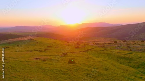 Sunset illuminates green hills and mountains with warm golden light, creating a tranquil and cozy atmosphere.