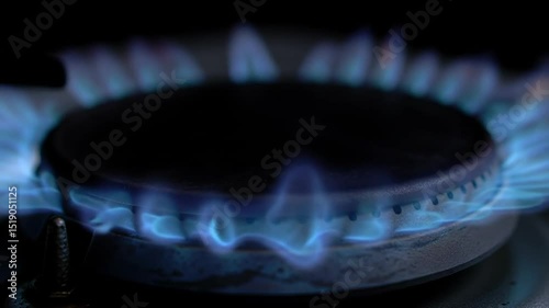 Close-up view of a gas stove burner igniting with blue flames in a dark kitchen setting