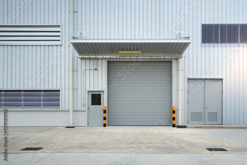 Exterior of industrial building. Construction for factory, store or warehouse. Include shutter door at front. Nobody empty space on concrete floor suit for product display or industrial background.