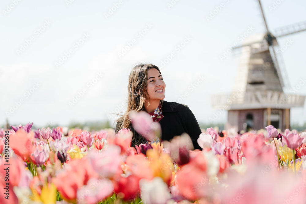 Fototapeta premium Woman Smiling in Front of Traditional Dutch Windmill and Tulips