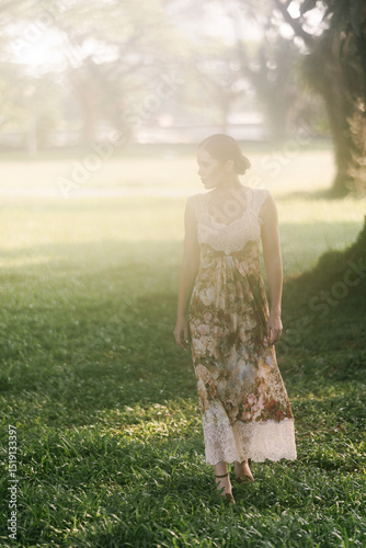 Elegant Caucasian woman with fair skin and dark hair posing in floral dress among morning mist and soft greenery. Aesthetic foggy dawn scene full of calm and natural beauty. photo