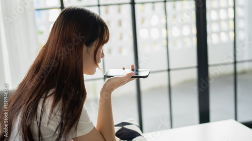 Photos Asian woman sitting using smartphone talking with friend by speakerphone