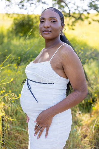 On a warm summer day, a beautiful pregnant woman embraces nature, proudly showing her baby bump. She is filled with love and anticipation for her child, radiating bliss and happiness