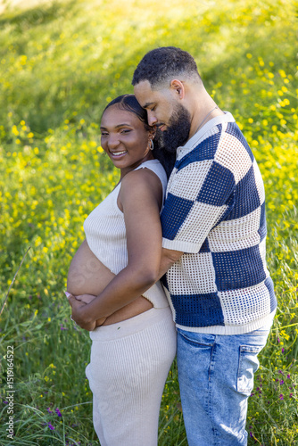 On a summer day, a loving African American couple cherishes the moment outdoors, surrounded by greenery, joyfully celebrating their pregnancy and embracing their journey together with warmth