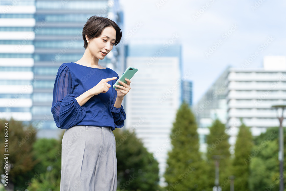 Fototapeta premium ビル街でスマートフォンを操作している女性