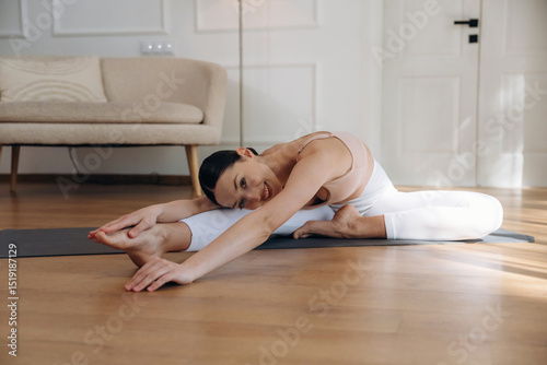 Flexibility exercise for legs. Young woman in fitness clothes is in the room