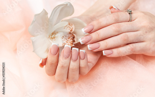Woman showing french manicure holding white orchid on pink background