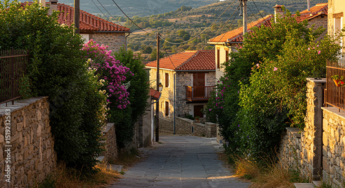 Quiet rural village street in a Mediterranean mountain town, traditional stone houses with red tiled roofs and wooden balconies, flowering bushes and dense greenery lining the narrow cobblestone road