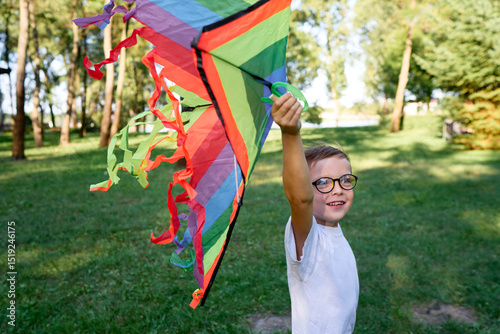 Little boy in white shirt running with kite on the field at summer day in the park