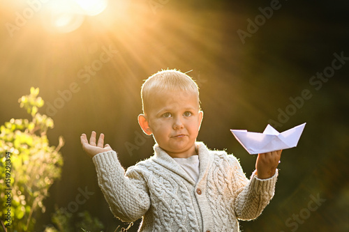 Little boy playing alone in the forest with a white paper boat. Peaceful childhood moment filled with imagination, solitude, and connection to nature.