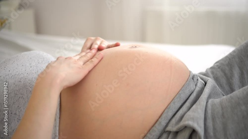 Pregnant woman lying on her back, gently touching her belly with visible baby movements. Close-up view of a real pregnancy moment.