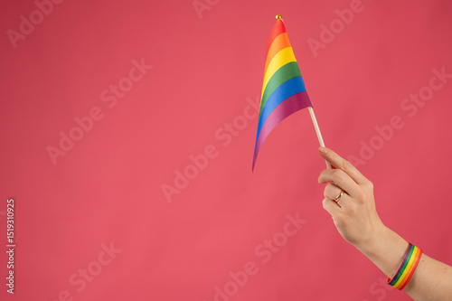 Woman with wedding ring holding rainbow flag on pink background. 