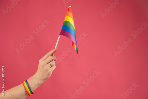 Woman with wedding ring holding rainbow flag on pink background. 