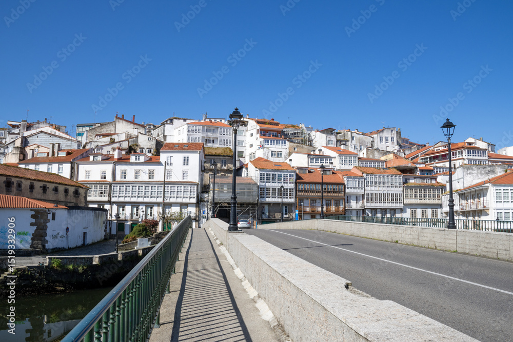 Obraz premium Traditional Galician white buildings seen from Ponte Vella bridge over Mandeo River in Betanzos, Spain, surrounded by lush greenery.