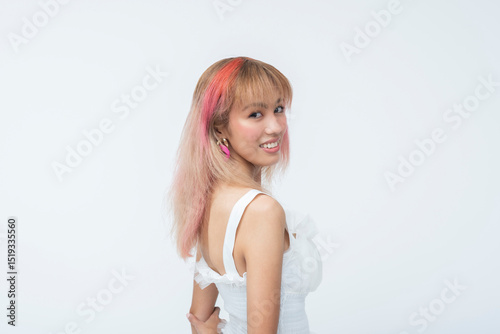 Southeast Asian woman with pastel hair glancing back gently while smiling in a sweet, relaxed, and charming way. Isolated on a light background.