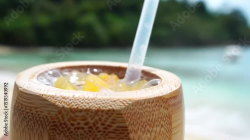 Filipino Coconut Kefir. Effervescent shot of young coconut water kefir - probiotic and tropical fruit SCOBY. Served in bamboo tumbler, Palawan beach setting.