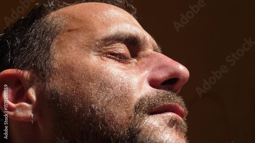 A young man sweats heavily while standing motionless under the summer sun