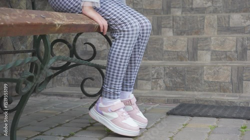 child sits on bench in sneakers, little girl in checked pants and white sneakers