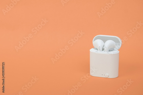 Modern wireless earbuds headphones isolated on orange background
