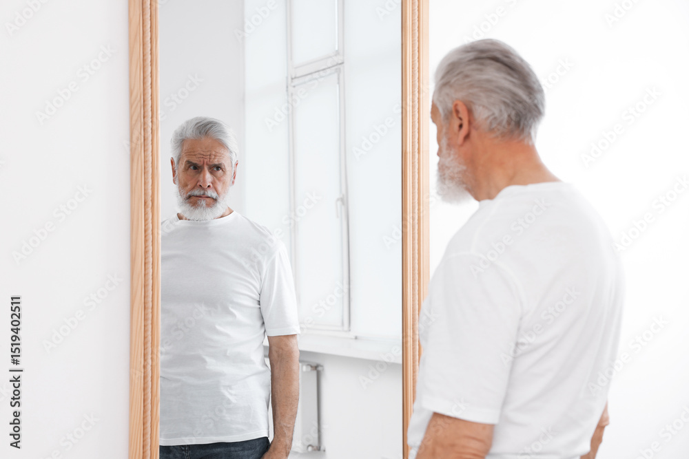 Obraz premium Handsome senior man looking at himself in mirror indoors
