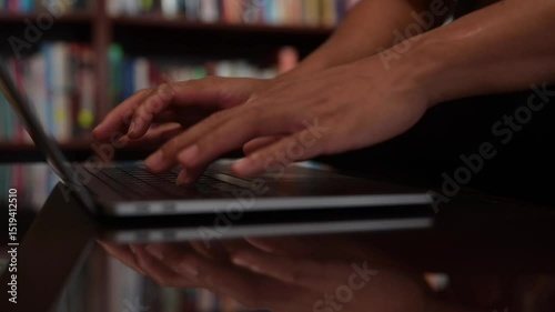 close up hand typing on computer laptop in home office with blurred book shelf and dark lighting background