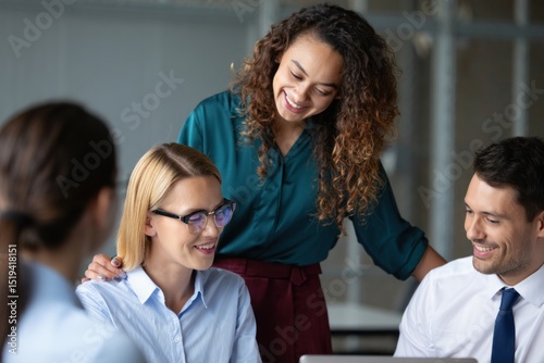 Four diverse young professionals collaborating happily in a modern office setting, showing smiles and supportive teamwork