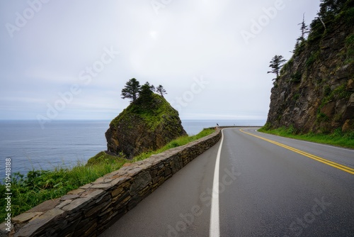 Curved coastal road with stone wall overlooking ocean and rocky cliffs under cloudy sky