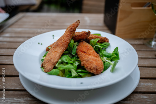 Foto Crispy breaded chicken strips on fresh green salad served in white plate outdoor