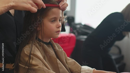 Little girl sitting in salon chair as hairstylist prepares hair for cut, capturing the grooming process in professional barbershop setting with focus and care