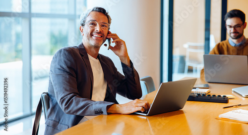 Confident professional man talking on the phone in office with laptop