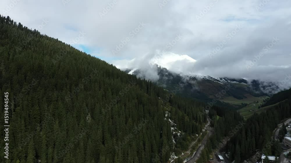 A dramatic aerial view of fog drifting through the snow-covered Zillertal Valley surrounded by coniferous forests.