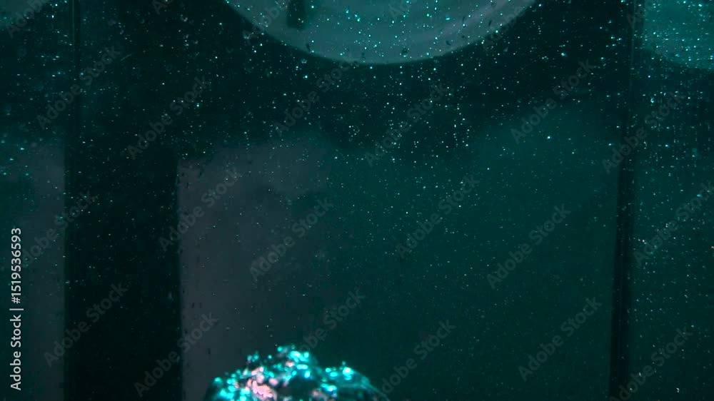 The texture of the water is a rumbling chaos with bubbles created by the air escaping outside in the blue light.