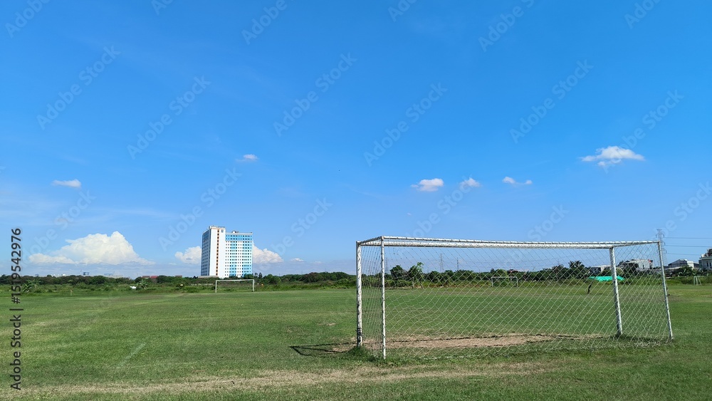 Fototapeta premium Soccer Field with Distant Skyscraper Under Blue Sky