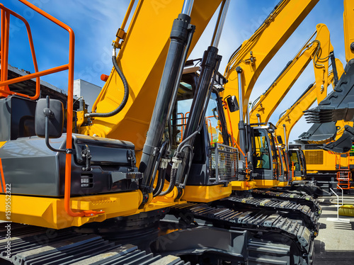 Heavy construction machinery lined up at a construction site under blue sky with minimal clouds