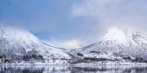 mountains and valleys formed by glaciers in winter, changing weather moods on the fjord between steep, snow-covered mountains in Troms, Norway. blue sky between dark clouds on the sky, snowy mountains