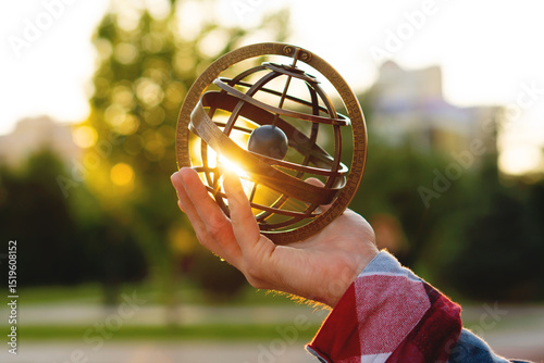 Person holding vintage armillary sphere illuminated by sunset rays. Astronomical instrument, spherical astrolabe