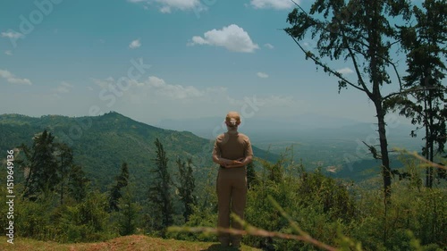 Young girl in cap stands on top of hill and admires majestic beauty of mountains. Back view. Mountains give sense of peace and tranquility and provide an opportunity to relax and reflect
