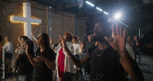 Diverse congregation raising hands in worship during church service, illuminated cross in background, spiritual connection and collective devotion in sacred space