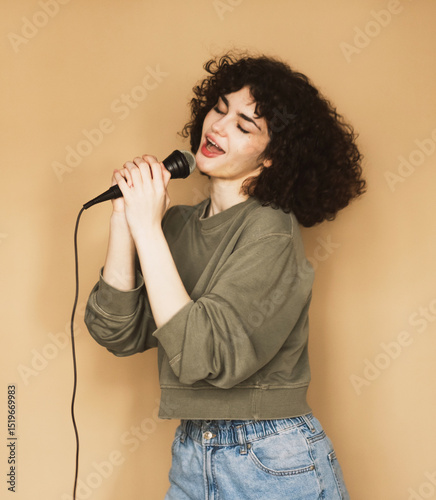 Cheerful curly-haired young woman sings songs into a microphone and dances.
