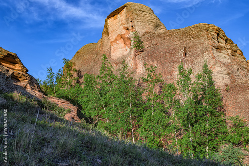 Powerful huge rock with green trees. Kazakh expanses, Mount Ku Egendybulak. Summer autumn landscape